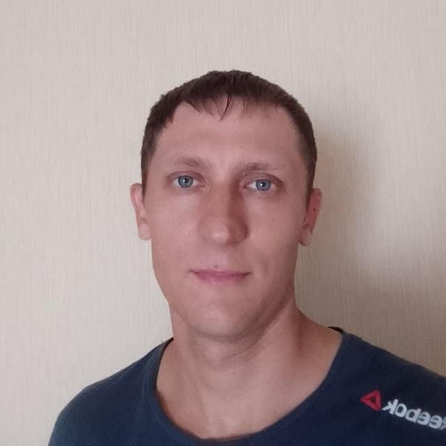 A man with short brown hair and blue eyes wearing a navy blue Reebok shirt.