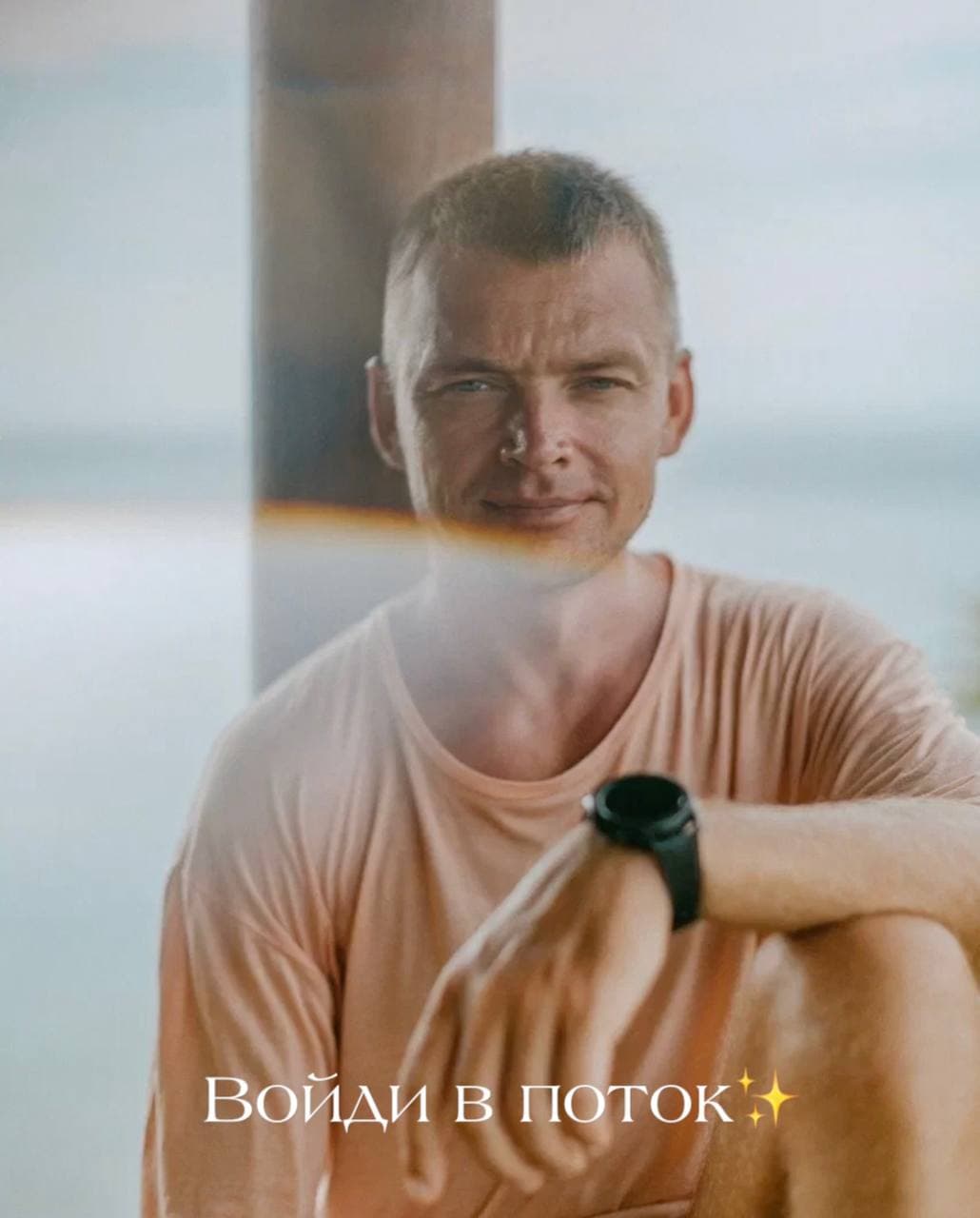 Smiling man in a peach t-shirt outdoors with a lens flare and Russian text overlay.